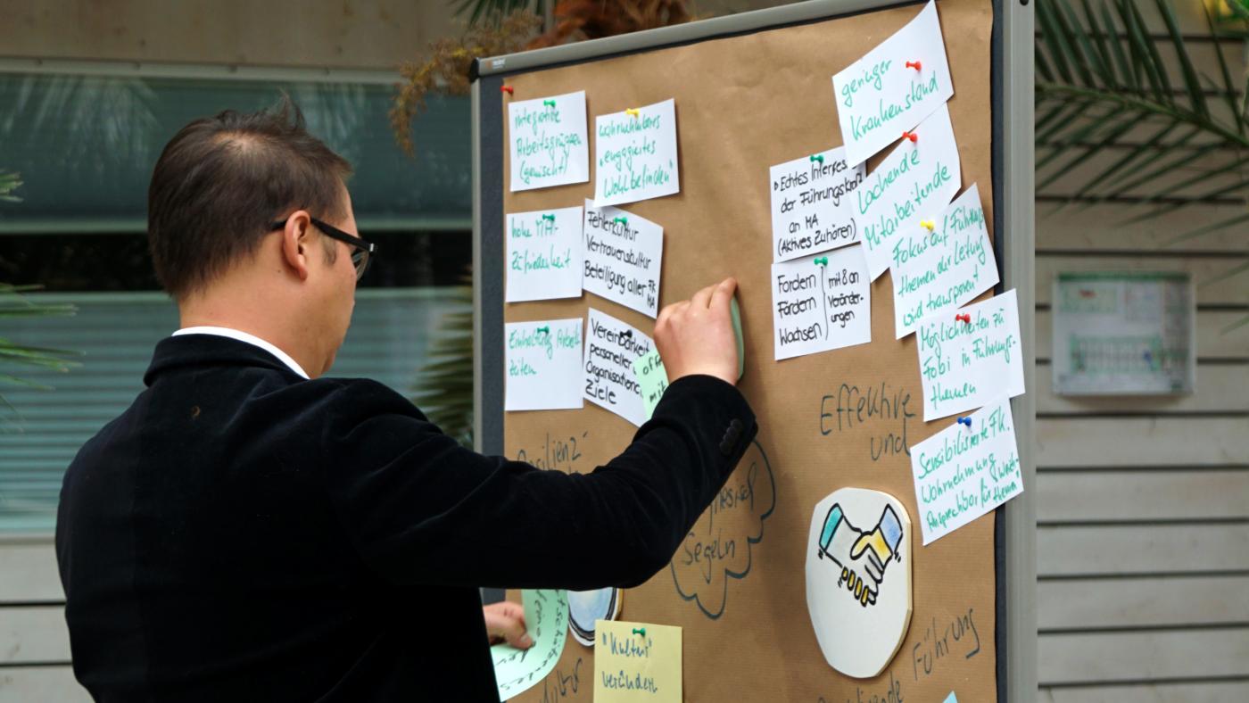 Ein Teilnehmer befestigt seine Notizen an einer Metaplanwand