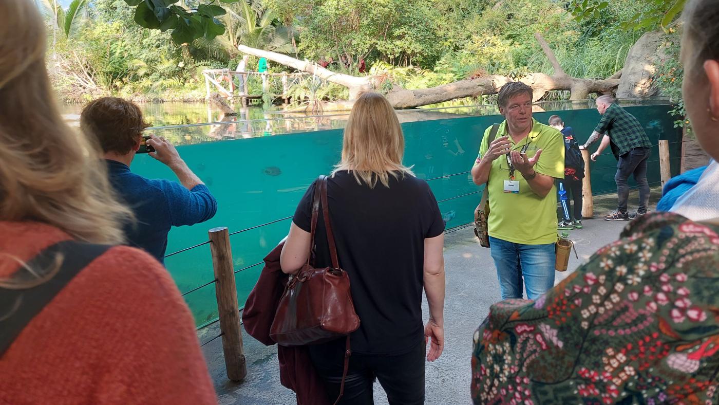 Die Besuchergruppe steht vor einem Wasserbecken im Zoo. 