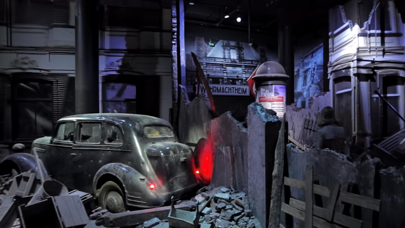 Nachgestellte Kriegsszene mit einem Auto, das zwischen Trümmern steht. 