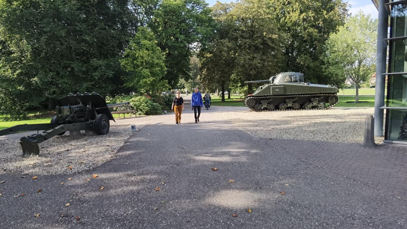 Zwei Gäste laufen auf die Villa Hartenstein zu. Im Hintergrund steht ein Panzer. 