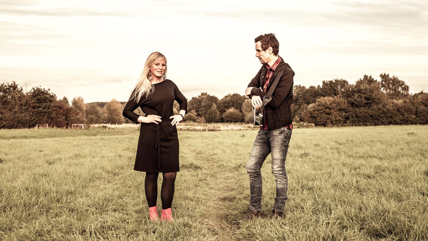 Eine Frau und ein Mann mit Gitarre stehen auf einer Weide