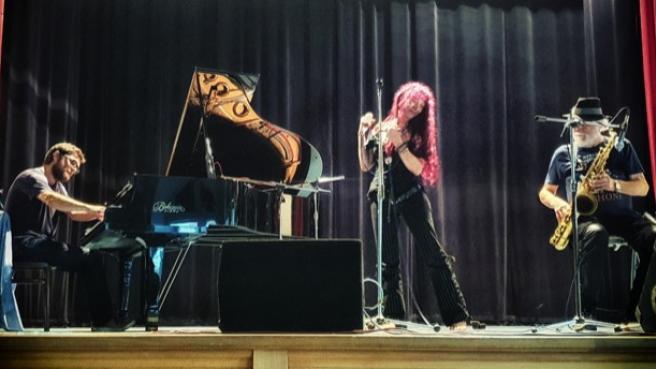 Von links nach rechts: Ein Pianist, eine Sängerin und ein Saxophonist auf einer Bühne