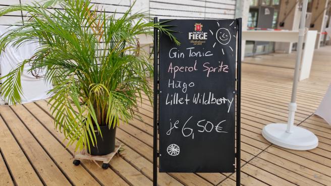 Auf einer Schiefertafel sind verschiedene Sommer-Cocktails aufgeschrieben, daneben eine Palme