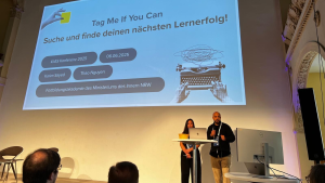 Eine Frau und ein Mann halten auf einem Podium einen Vortrag